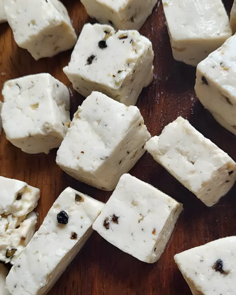 Cubes of PANEVO Black Pepper paneer on a dark wooden board, cracked peppercorns visible inside